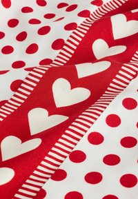 Weißer Stoff mit roten Punkten und einem roten vertikalen Streifen, der weiße Herzen sowie weiße und rote Streifen an den Rändern zeigt.