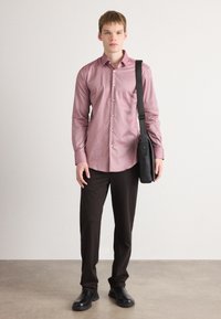 Camicia a quadri rossa e bianca con bottoni, indossata con pantaloni scuri e scarpe nere. Una borsa a tracolla nera è appesa alla spalla.