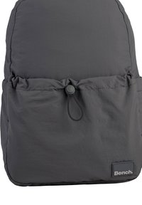 Gray soft fabric backpack featuring a gathered lower section, adjustable pull cord, and a logo patch at the bottom.