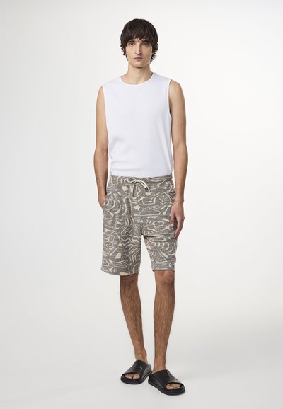 Vit ärmlös ribbad skjorta, mönstrade beige och grå shorts med dragsko, bärs med svarta flatsandaler. Enkelt, avslappnat sommaroutfit.