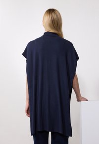 Navy blue oversized top with short sleeves, made of soft fabric, featuring a high collar and flowing design. Simple and minimalistic style.