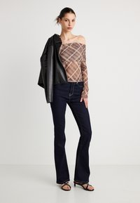 Top de cuadros beige y marrón con los hombros descubiertos, combinado con vaqueros acampanados azul oscuro. La modelo lleva una chaqueta de cuero negra sobre un hombro.