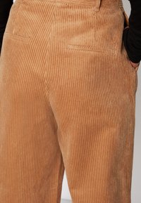 Corduroybyxor i en varm tan-färg, med vertikala ribbor, en åtsittande midja och två bakfickor. Mjuk textur med en slät yta.