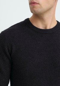 Dunkelgrauer strukturierten Pullover mit einem gerippten Strickdesign und einem Rundhalsausschnitt, der eine taillierte Form und weichen Stoff aufweist.