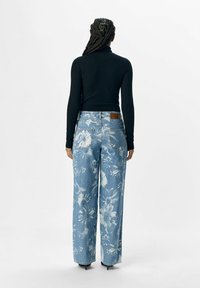Jeans de pierna ancha de lavado claro con un estampado floral azul, con una cintura alta y una etiqueta de cuero marrón en la parte posterior de la cinturilla.