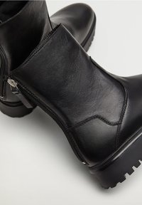Bottes de cheville en cuir noir avec une finition texturée, dotées d'une fermeture éclair sur le côté et d'une semelle robuste à motif pour une meilleure adhérence.