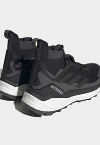 Schwarze Sportschuhe mit einem gestrickten Obermaterial, ausgestattet mit einer weißen, gepolsterten Sohle, strukturiertem Design und einem markanten Logo der Marke an der Seite.