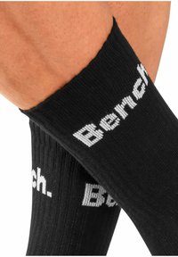 Schwarze knielange Socken aus geripptem Stoff mit dem weißem "Bench."-Logo, das deutlich am Bündchen zu sehen ist.