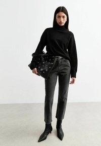 Svart polotröja, grå höga jeans, svarta spetsiga ankboots och en svart väska med dekorativa silveröglor.