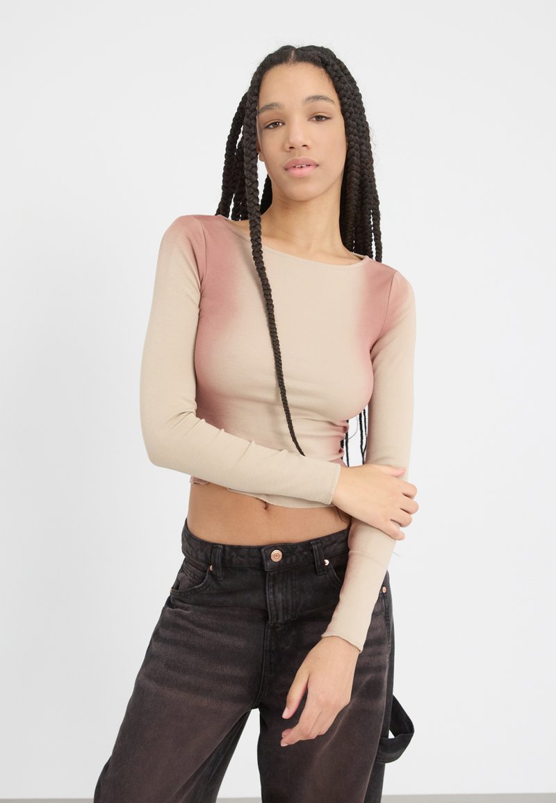 Langermet topp i beige og rosa ombre design med en tettsittende fasong. Kombinert med høyhårede svarte jeans med kobberknapper.