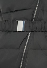 Μαύρο μπουφάν με γυαλιστερή ασημένια πόρπη ζώνης, ορατά ραψίματα και λεπτομέρεια με φερμουάρ στην μπροστινή πλευρά. Λείο, καπιτονέ υλικό.