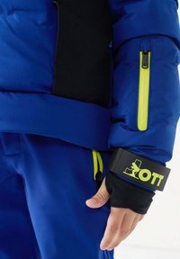 Herenjas met isolatie in blauw en zwart, voorzien van gele ritsen, een aansluitende manchetten met logodetail en een glad, gewatteerd oppervlak.