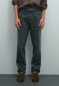Jeans in denim grigio scuro con taglio dritto, design classico a cinque tasche, dettagli cuciti, abbinati a scarpe in pelle scamosciata marrone.