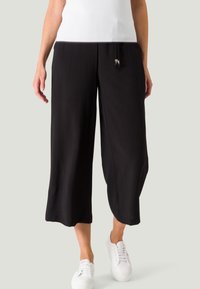 Zwarte culottes van soepel stof, met een relaxte pasvorm, cropped lengte en een tailleband met trekkoord en metalen accenten. Gemaakt in combinatie met witte sneakers.