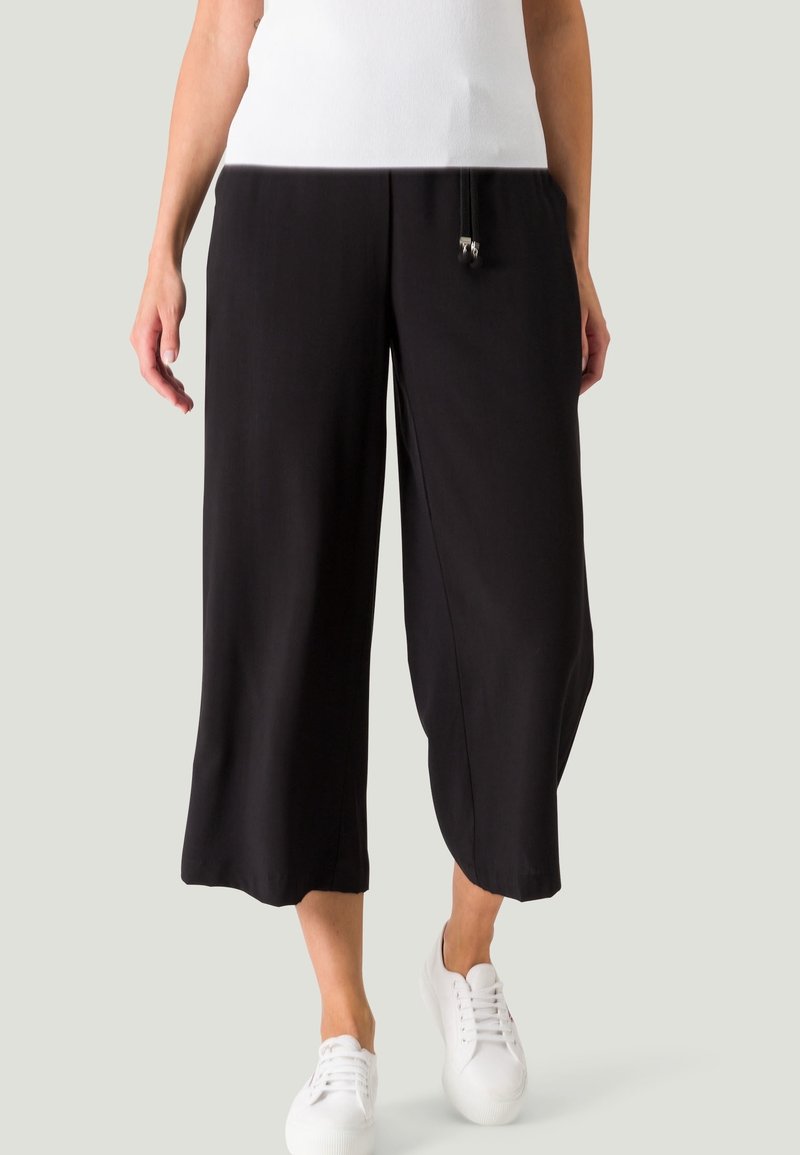 Zwarte culottes van soepel stof, met een relaxte pasvorm, cropped lengte en een tailleband met trekkoord en metalen accenten. Gemaakt in combinatie met witte sneakers.