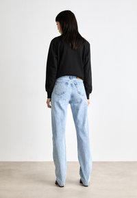 Sudadera negra, jeans de tiro alto de color azul claro, diseño de pierna recta, textura suave, vista trasera, detalles mínimos, sin logotipos visibles.