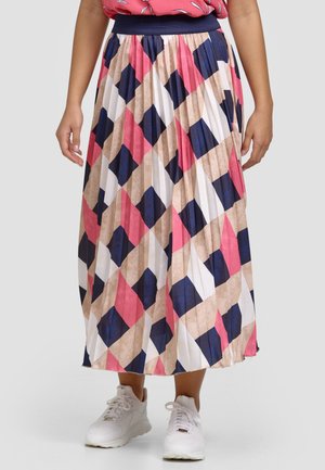 Jupe midi plissée à motif géométrique bleu marine, rose, beige et blanc portée avec des baskets blanches et un haut corail.