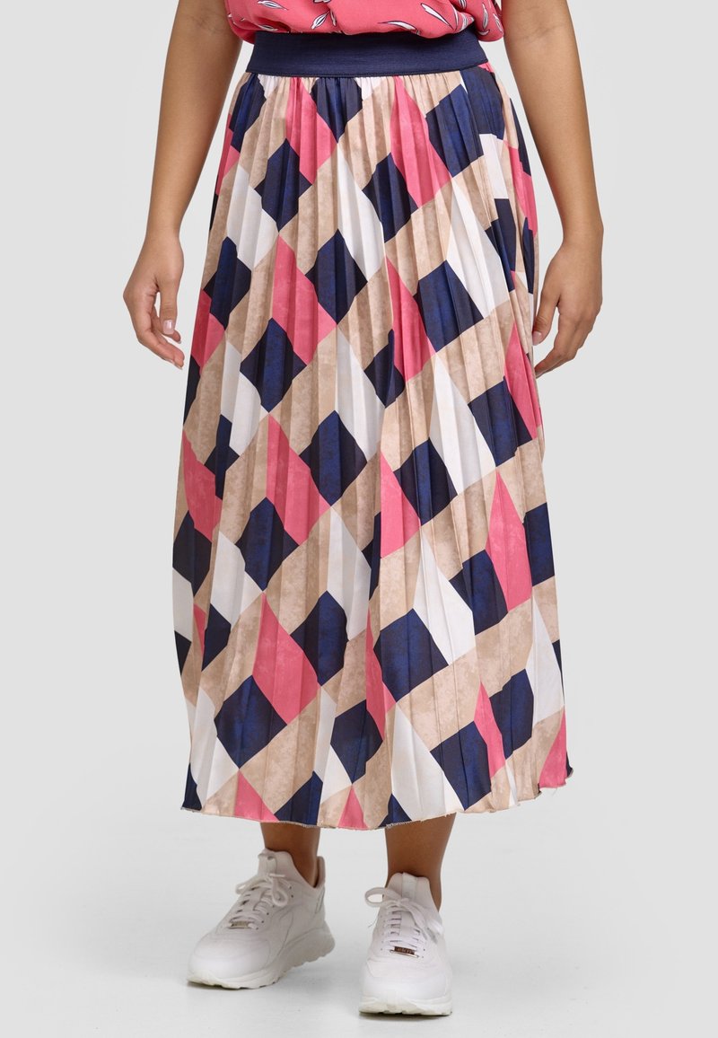 Jupe midi plissée à motif géométrique bleu marine, rose, beige et blanc portée avec des baskets blanches et un haut corail.