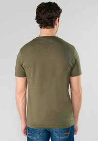 Camiseta de manga corta color verde olivo con cuello redondo, hecha de una tela suave, mostrada desde la parte de atrás, mostrando un diseño simple y ajustado.