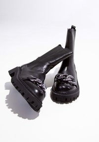 Bottines noires en cuir avec une semelle épaisse, ornées d'une chaîne en argent décorative sur le bout et d'une finition lisse.