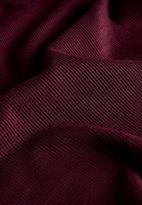 Tissu côtelé rouge foncé avec de fines rayures verticales et des plis doux créant des ombres courbées et une profondeur de texture.