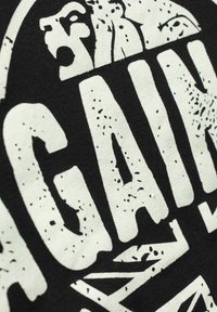 Lähikuva mustasta kankaasta, jossa on suuret valkoiset kuluneet kirjaimet "GRAN" ja osia ympäröivistä kirjaimista pyöreässä kuviossa.