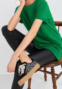 T-shirt verde in cotone con maniche arrotolate, abbinato a leggings in ecopelle neri e sneakers nere con pois bianchi e suola beige.