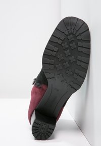 Stivale alla caviglia in suede con tomaia nera e parte bassa bordeaux. Presenta una suola in gomma testurizzata con un battistrada decorato per una presa sicura. Chiusura laterale con zip.