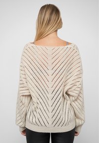 Weißer, locker gestrickter Pullover mit einem Chevron-Muster, weit geschnittenen Ärmeln und rundem Ausschnitt. Strukturierte Oberfläche mit offenen Maschen und geripptem Saum.