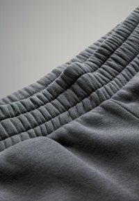 Tessuto elasticizzato grigio con vita arricciata, caratterizzato da una texture morbida e una lucentezza sottile. Ingrandimento della morbidezza e del design del materiale.