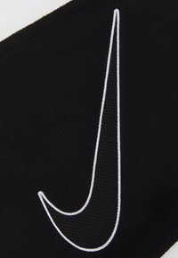 Sort fleece-stof med et fremtrædende hvidt broderet Nike-swoosh-logo. Glat tekstur, buet design og synlige forstærkede syninger.