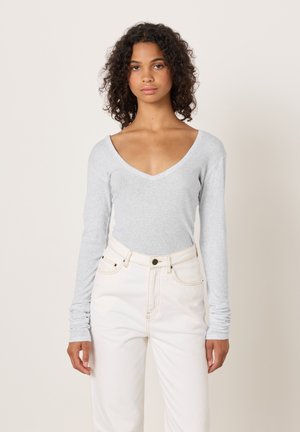 Long-sleeve gray top with a deep V-neck, fitted design, made of soft fabric, paired with high-waisted white jeans. Minimalist style.