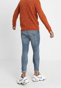 Pull orange texturé, jean slim bleu clair avec détails usés, et baskets blanches athlétiques avec accents noirs.