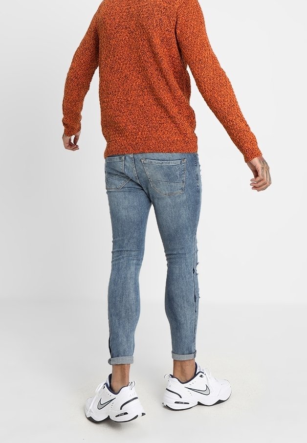 Pull orange texturé, jean slim bleu clair avec détails usés, et baskets blanches athlétiques avec accents noirs.