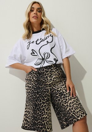 T-shirt bianco con grafica nera "je t'aime" e un fiocco, abbinata a pantaloni corti leopardati fino al ginocchio. Tessuto liscio, vestibilità ampia, modelli audaci.