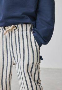 Stribede bukser i creme og marineblå med et tekstureret stof, elastisk talje og snor lukning. Lille mærke ved siden.