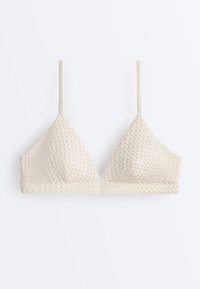 Cremefarbener, strukturierter Bralette mit dreieckigen Cups, dünnen verstellbaren Trägern und breitem Unterbrustband vor weißem Hintergrund.