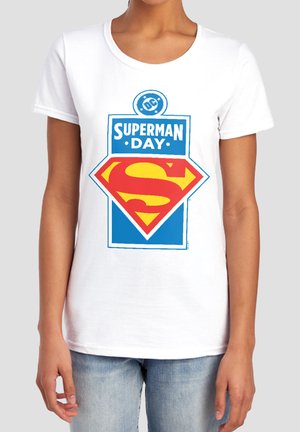 White T-shirt with a large blue and red Superman logo and "Superman Day" text worn by a person in blue jeans against a plain background.