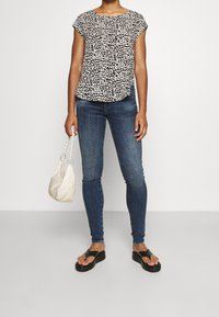 Haut en imprimé léopard noir et blanc, jeans en denim, sandales noires à brides et sac à épaule crème avec une surface texturée et une chaîne.