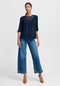 Navy blue blouse with lace detailing at neckline, three-quarter sleeves, and lightweight fabric, paired with wide-leg blue jeans and beige heels.