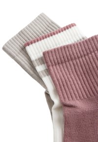 Trois paires de chaussettes en maille côtelée beige, blanche avec des rayures beiges et mauves, et mauve uni empilées sur un fond blanc.