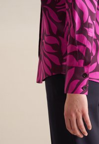 Koszula z długim rękawem w ciemnofioletowym kolorze z wyraźnymi różowymi wzorami liści, z zapięciem na guziki przy mankietach i gładkim wykończeniem materiału.