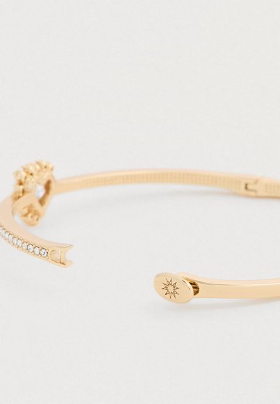 Kuldse tooniga mansetinõel käevõru tekstureeritud rihma ja rhinestone kaunistustega, sulgemiskohal dekoratiivse tähegravaaziga.