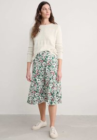 Cream knit sweater with a textured diamond pattern, paired with a green floral-print midi skirt and beige sneakers.