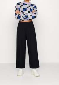 Pull tricoté multicolore avec un motif à carreaux en lavande, bleu, vert et noir ; associé à un pantalon large taille haute noir.