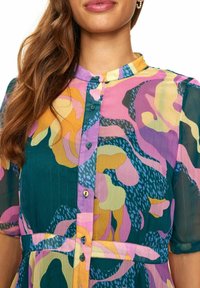 Rochie cu butoni multicolor, având o bază verde, modele abstracte în roz, galben și albastru, cu guler înalt și mâneci scurte.
