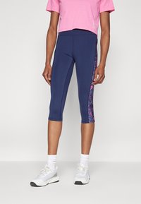 Navy capri leggings with a pink floral side panel, paired with a cropped pink t-shirt and white athletic shoes. Smooth, stretchy material.