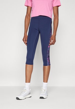 Marineblå capri leggings med en lyserød blomster sidepanel, parret med en cropped lyserød T-shirt og hvide træningssko. Glat, strækbart materiale.