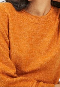 Orange knitted sweater with a textured finish, featuring a ribbed neckline and long sleeves. Close-up view of the fabric's softness.