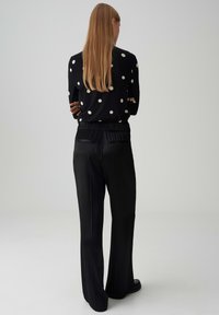 Pantalons larges noirs avec taille élastique, associés à un pull noir à pois blancs, vus de dos.